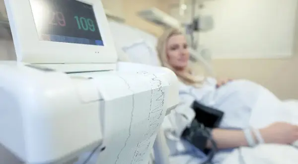 Monitor KTG z wydrukiem zapisu i ciężarną w tle.